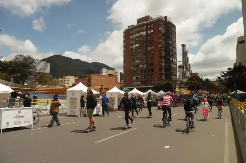 Ciclistas, patinadores y peatones en una avenida cortada al tráfico de Bogotá, con carpas blancas y edificios altos