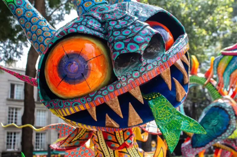Primer plano de un alebrije gigante con ojos naranjas, dientes y motivos de colores en el Paseo de la Reforma