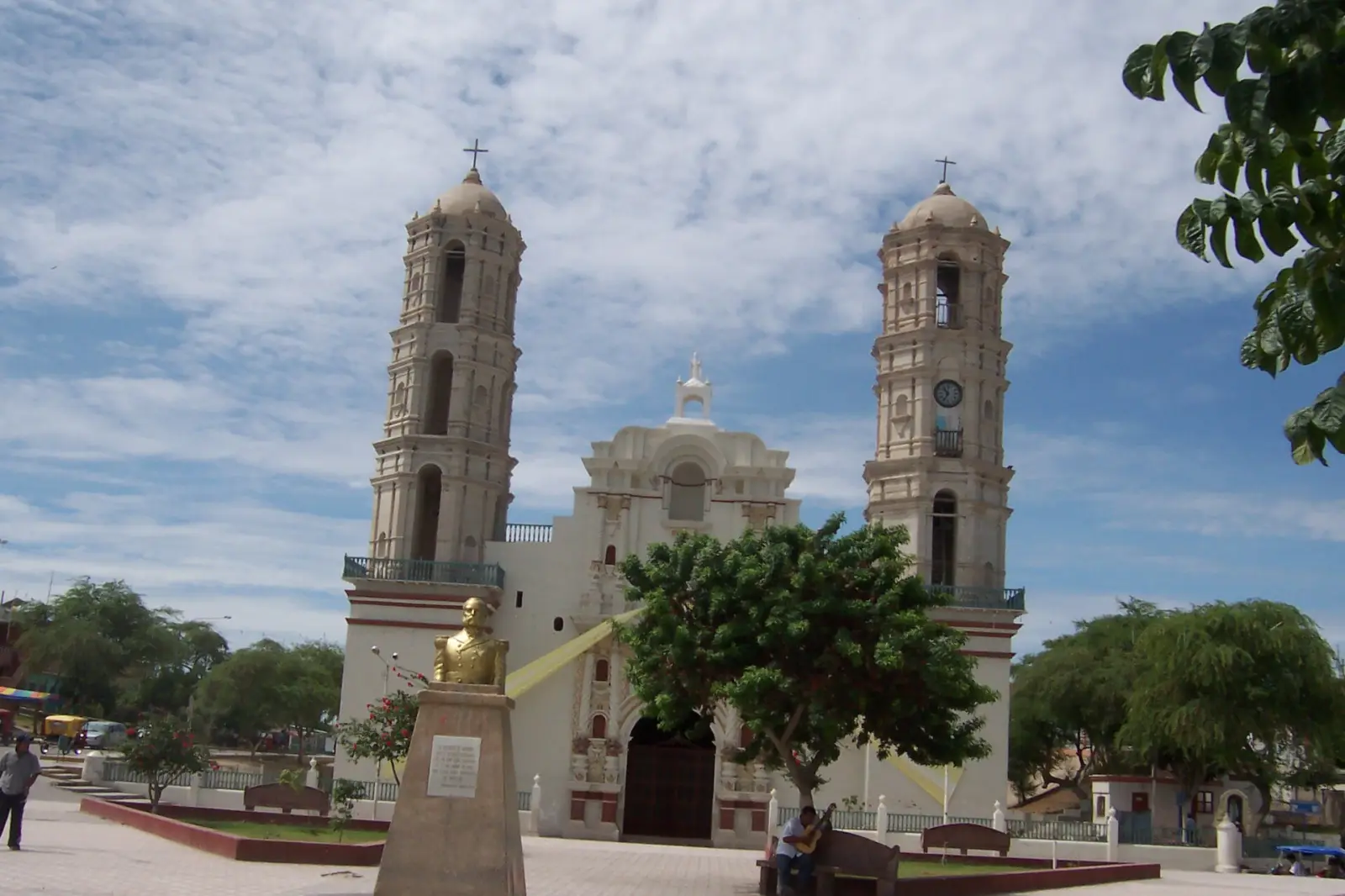 Catedral de Sechura, con dos torres blancas, junto a una plaza con árboles bajo un cielo azul