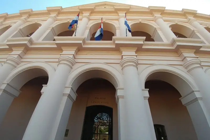 Fachada blanca con arcos del Cabildo de Asunción, con banderas de Paraguay en el balcón superior