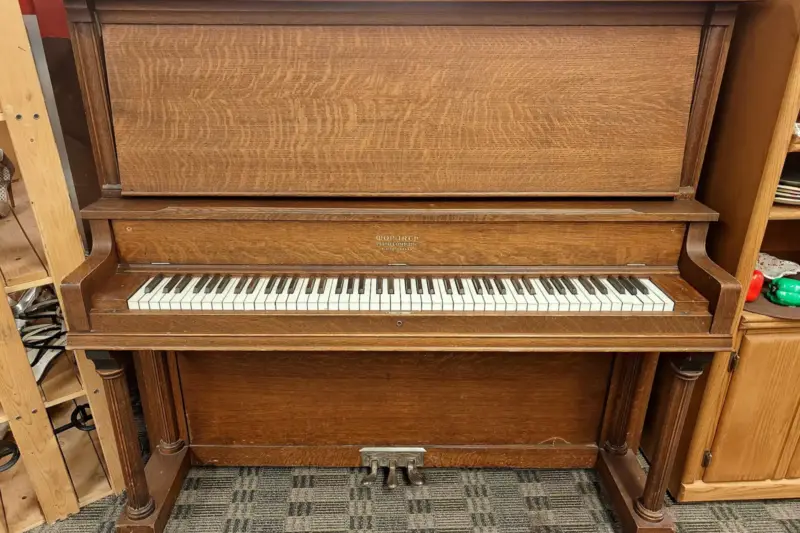 Piano vertical antiguo de madera oscura con la tapa del teclado abierta