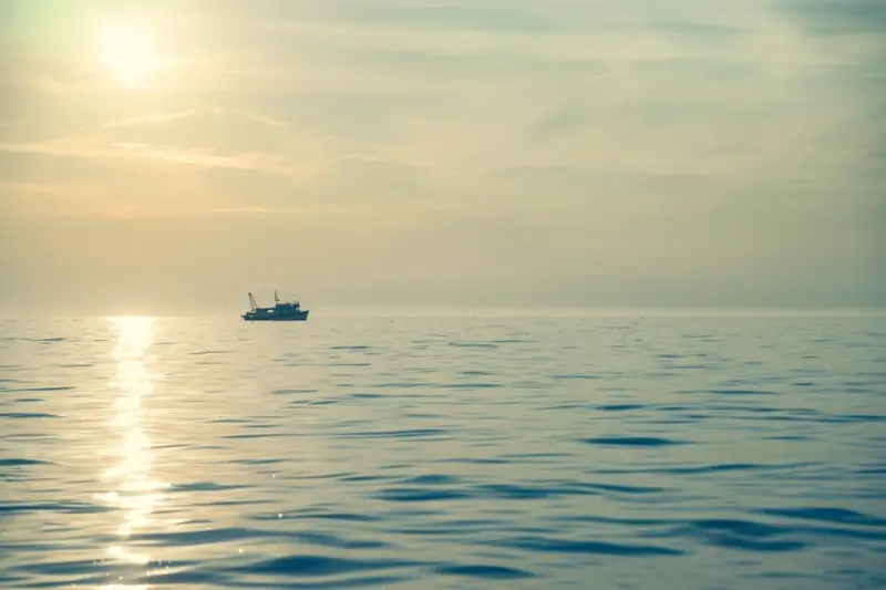 Embarcación de pesca artesanal a la deriva en alta mar bajo un cielo despejado.