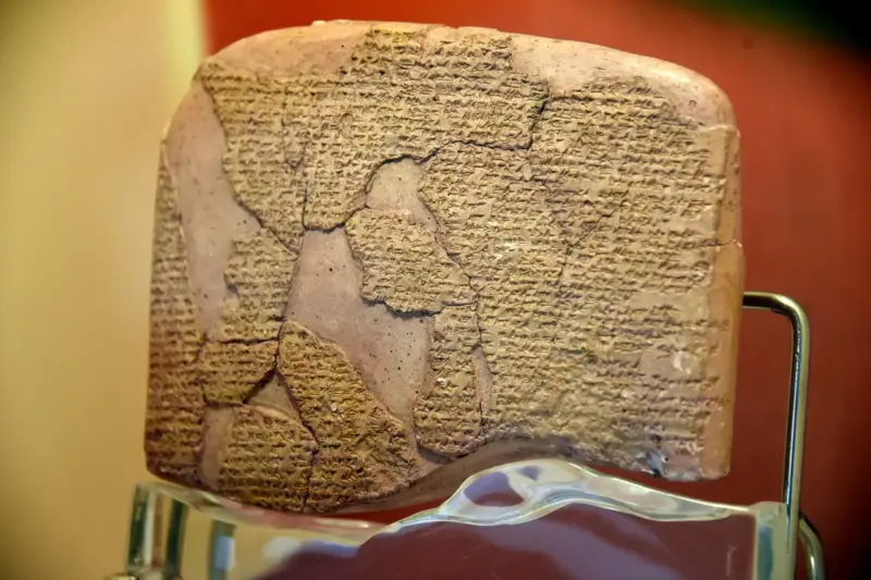 Tablilla de arcilla con escritura cuneiforme, agrietada y restaurada, expuesta sobre un soporte en un museo
