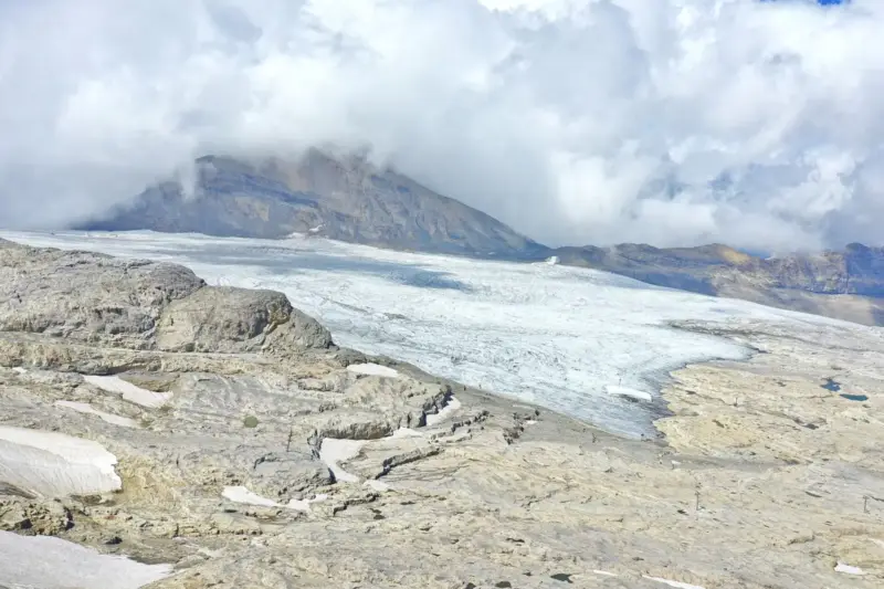 Lengua de hielo del glaciar de Tsanfleuron entre rocas calizas, con montañas cubiertas de nubes al fondo