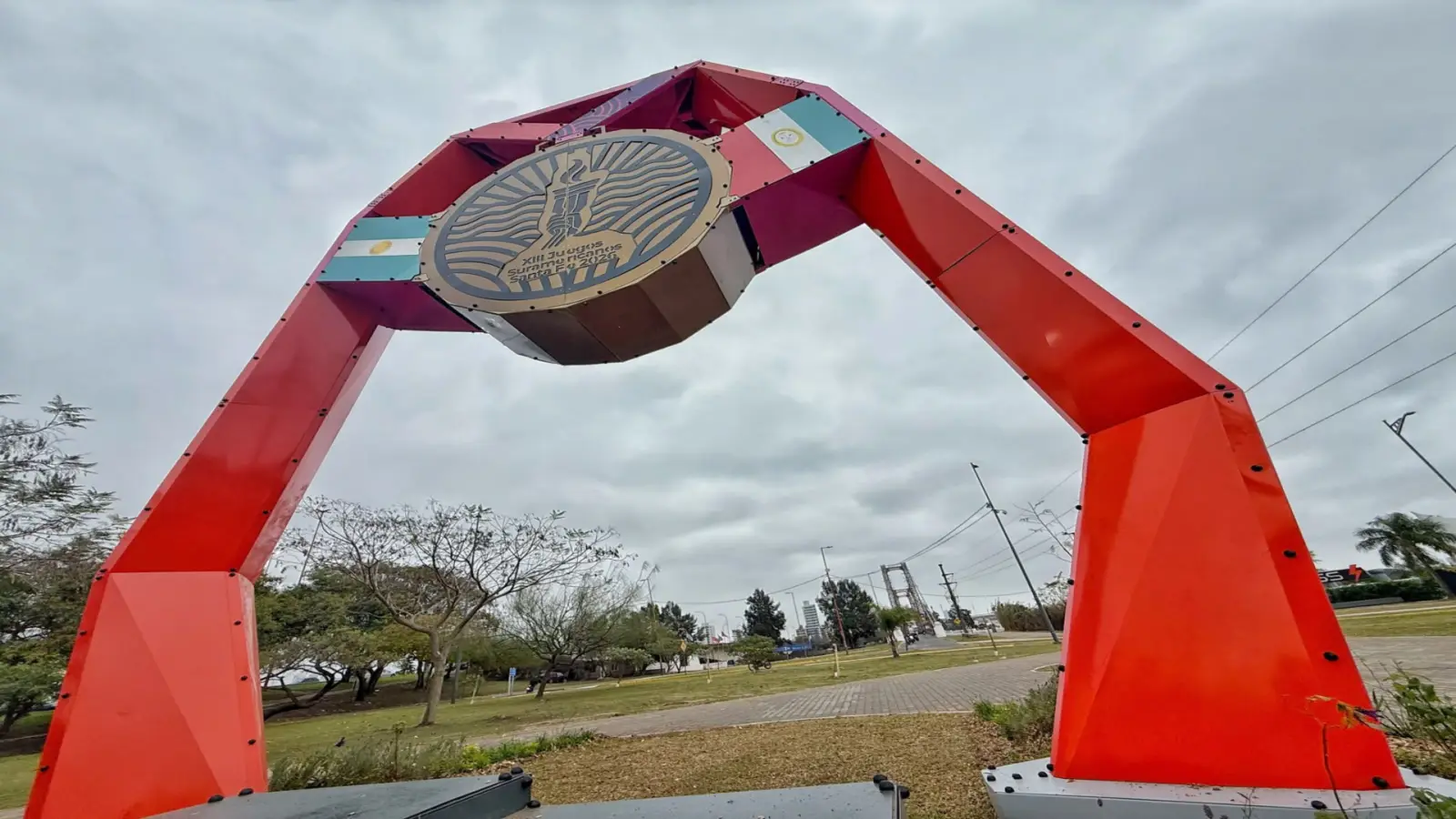 Gran arco rojo con el emblema de los Juegos Suramericanos 2026 y banderas argentinas en un parque de Santa Fe