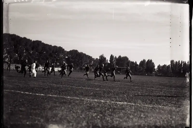 Campo de fútbol vacío al atardecer con un balón sobre la hierba y bancos al borde del terreno de juego.