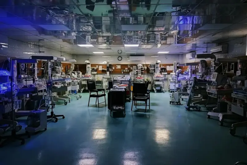Pasillo de una unidad de cardiología pediátrica con una incubadora y un monitor cardíaco junto a una ventana con luz de…