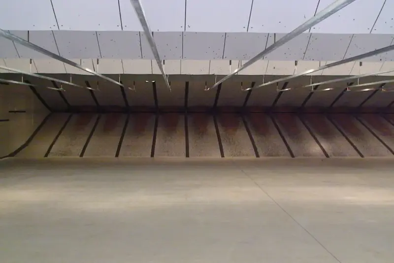 Galería de tiro vacía con una pistola sobre el banco de tiro, casquillos y una diana al fondo.
