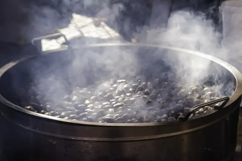 Castañas asadas en una plaza de pueblo al atardecer, con vecinos reunidos en otoño