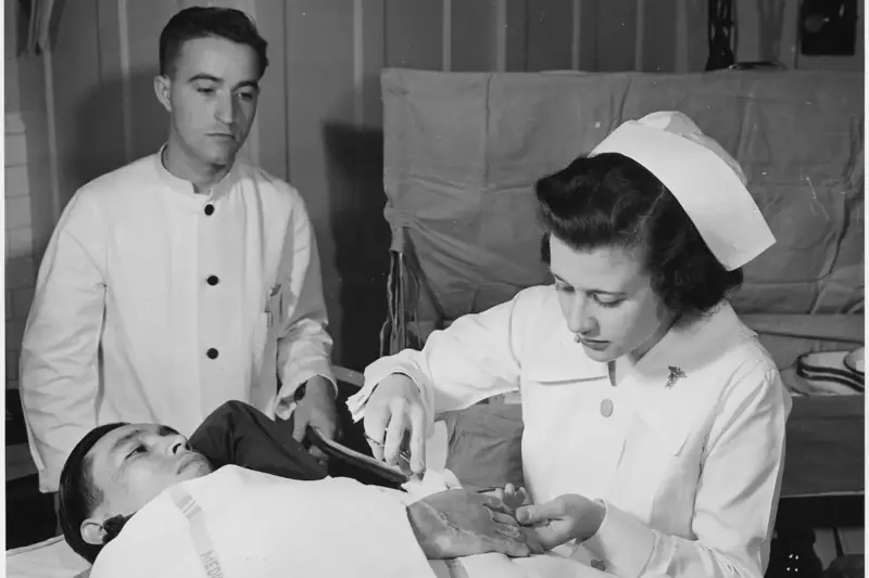 Manos de una cuidadora colocando un apósito blanco sobre una mesa de una sala de hospital con luz natural.