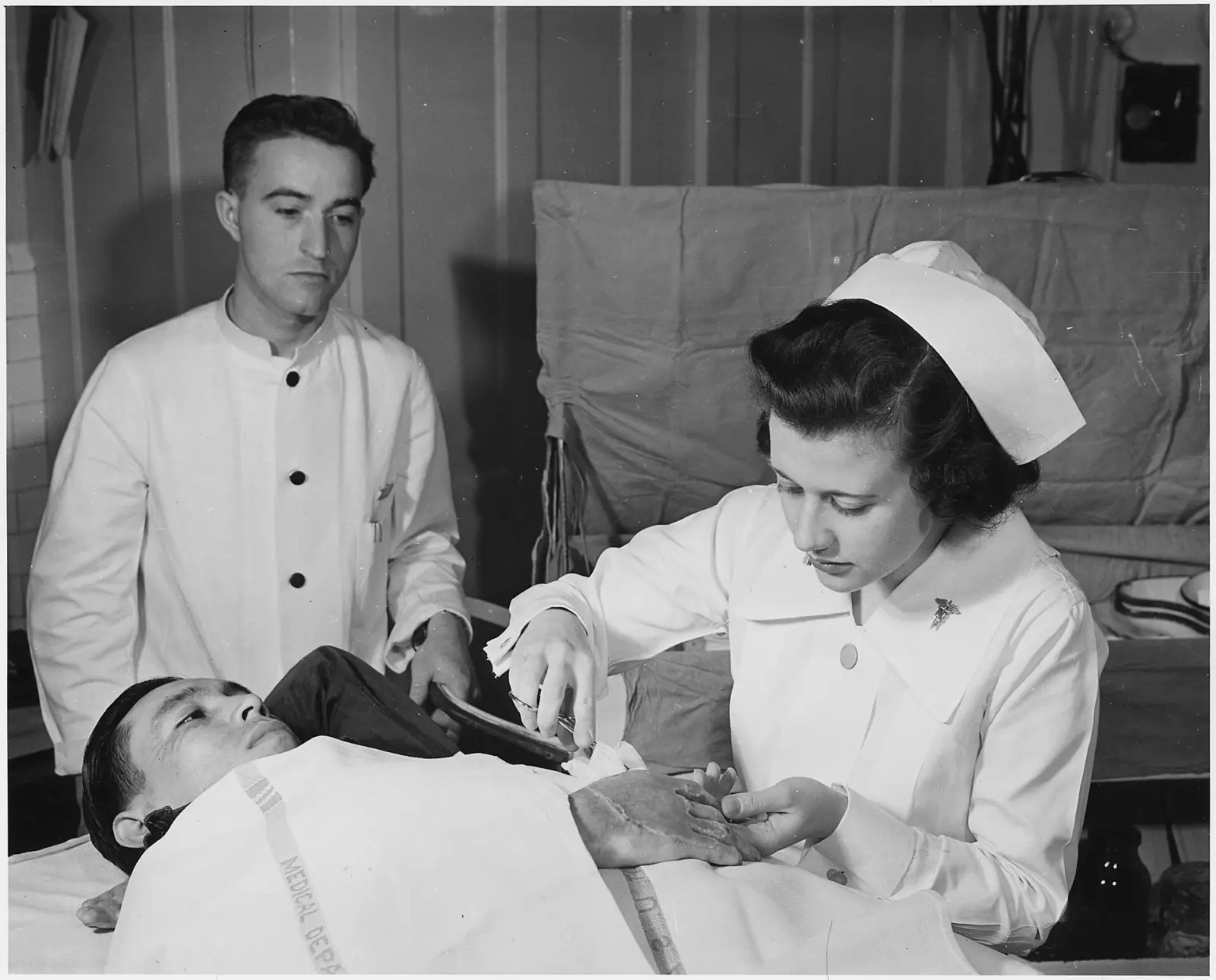 Manos de una cuidadora colocando un apósito blanco sobre una mesa de una sala de hospital con luz natural.
