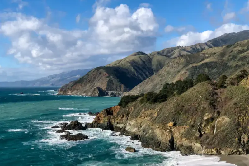 Costa rocosa de California con olas rompiendo con fuerza contra las rocas durante el atardecer.