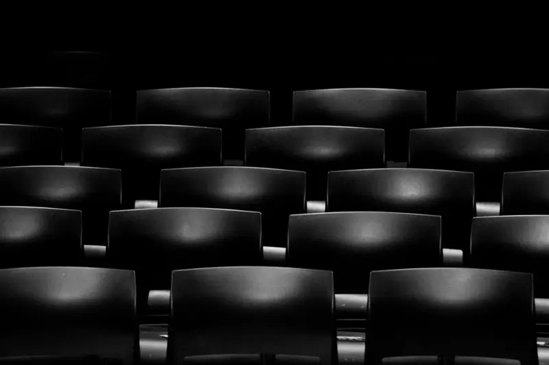 Interior de un teatro con butacas rojas vacías frente a un escenario iluminado.