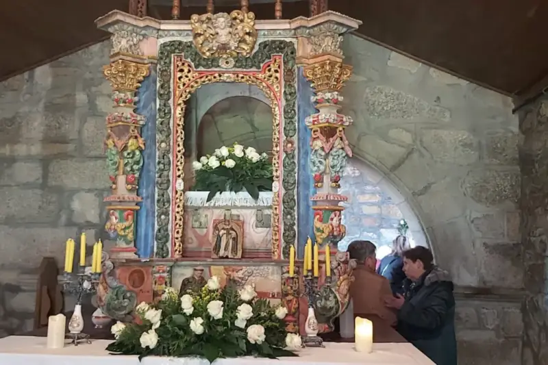 Interior de una iglesia rural de Galicia con bancos de madera y luz natural, durante un acto de homenaje a un sacerdote.