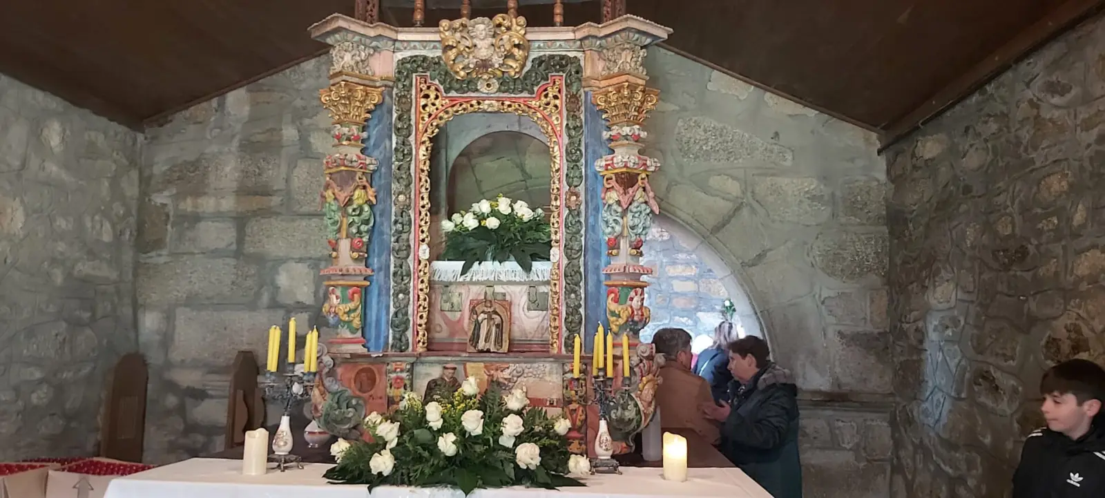 Interior de una iglesia rural de Galicia con bancos de madera y luz natural, durante un acto de homenaje a un sacerdote.
