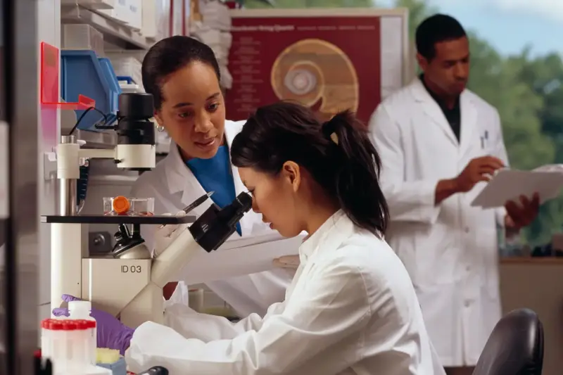 Mano enguantada sostiene un tubo de muestra en un laboratorio de investigación con luz natural.