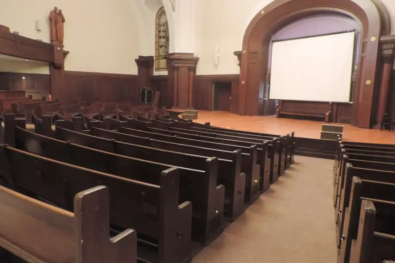 Escenario de una sala de conciertos con sillas de orquesta, atriles y butacas vacías, iluminado para una función