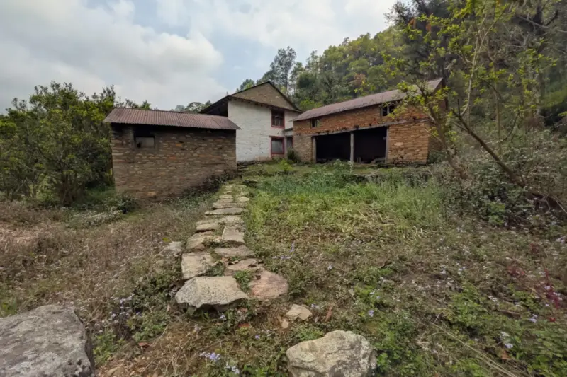 Casa rural antigua de piedra en un pueblo pequeño, con tejado parcialmente renovado y una escalera apoyada en la fachada.