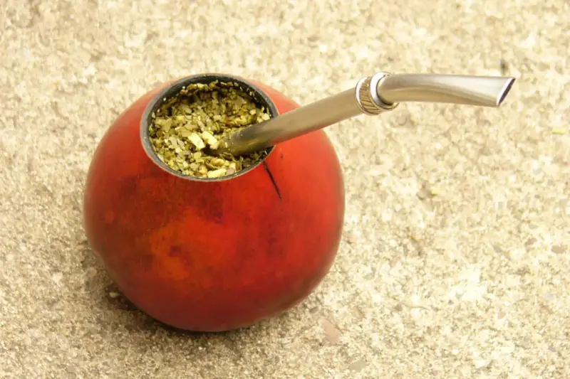 Joven preparando una montañita de yerba en un mate sobre una mesa durante un concurso en un museo.