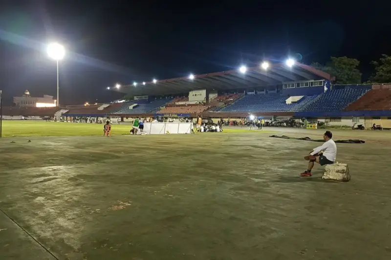 Estadio de fútbol de noche con el césped iluminado y una bandera de córner en primer plano