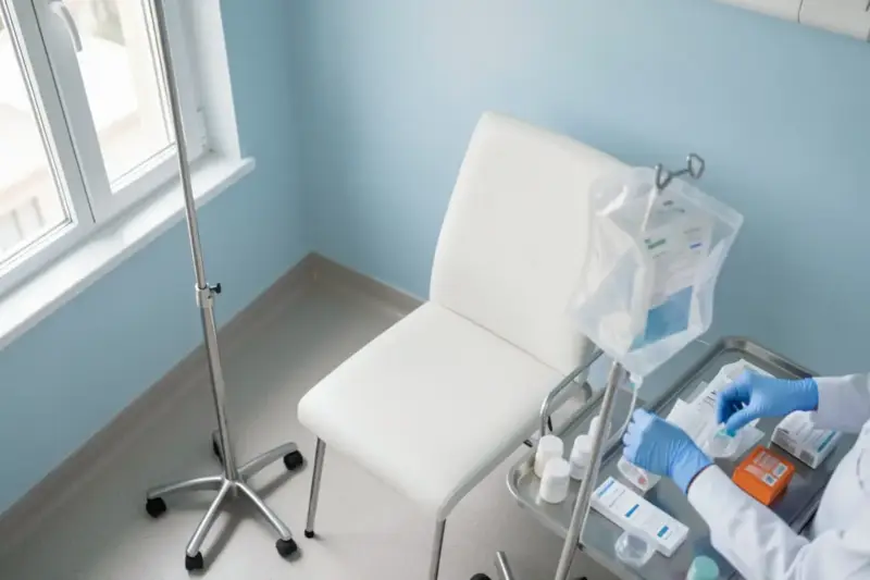 Sala de tratamiento de un hospital con una silla vacía, un soporte de suero y material sanitario preparado.