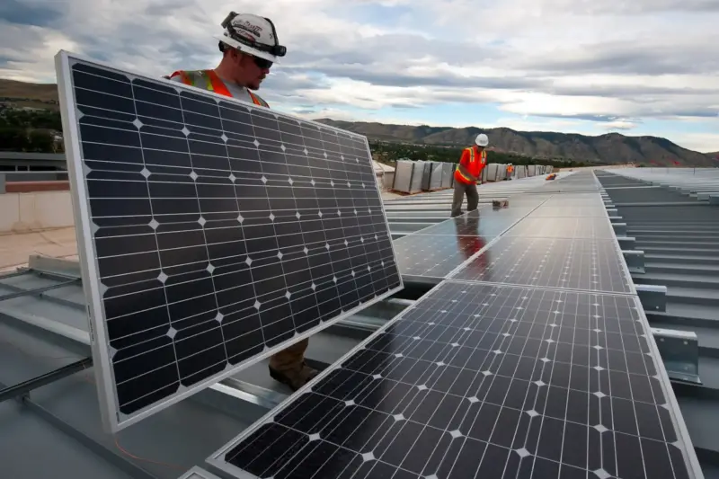 Paneles solares junto a una antena de telefonía en una colina rural, con un técnico trabajando al atardecer