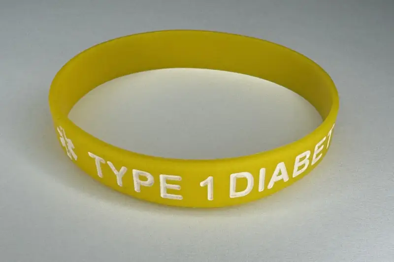 Pulsera médica de silicona con iconos de alérgenos y código QR sobre una superficie neutra.