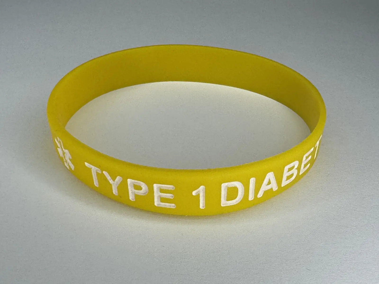 Pulsera médica de silicona con iconos de alérgenos y código QR sobre una superficie neutra.