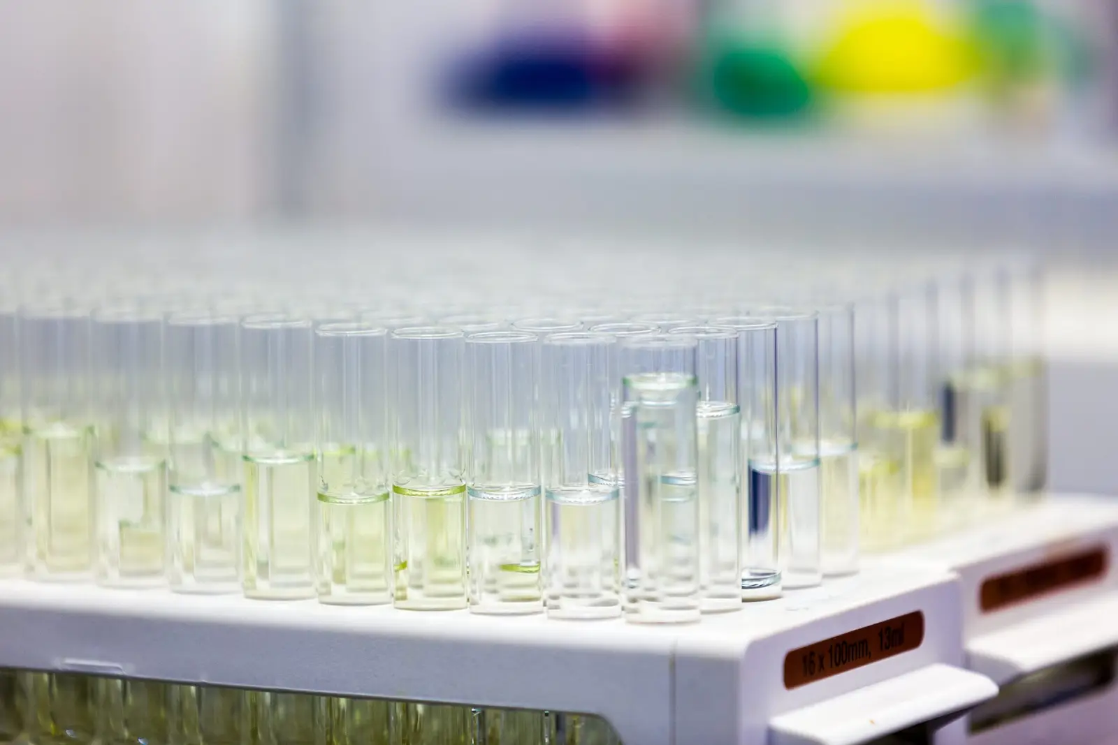 Vial de reacción química iluminado sobre una mesa de laboratorio, con un investigador al fondo.