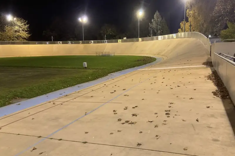 Ciclista de pista en plena curva de un velódromo cubierto, con las gradas desenfocadas al fondo.