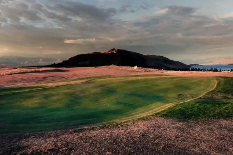 Campo de golf con césped verde y jugadores caminando hacia la casa club al atardecer.