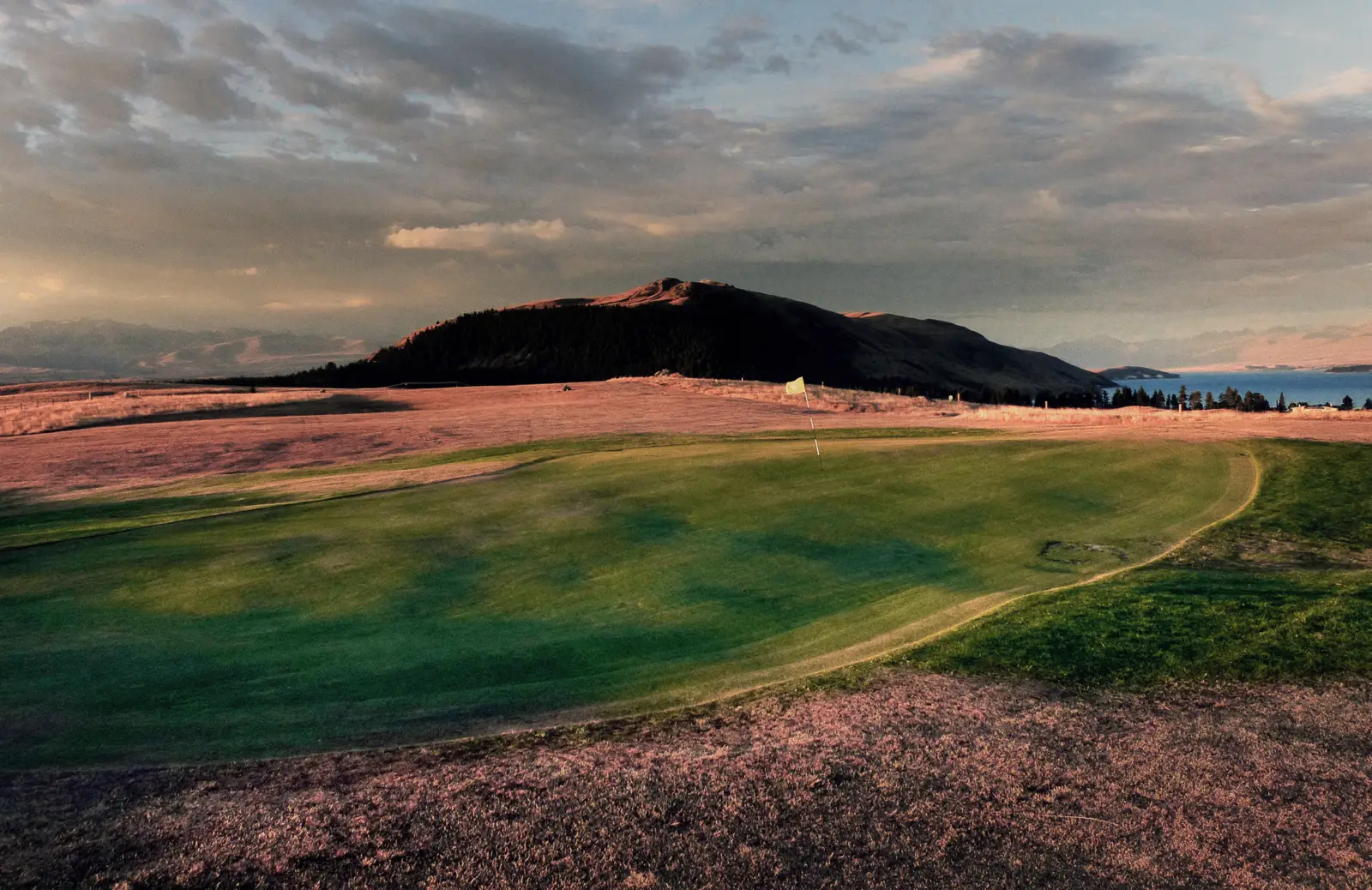 Campo de golf con césped verde y jugadores caminando hacia la casa club al atardecer.