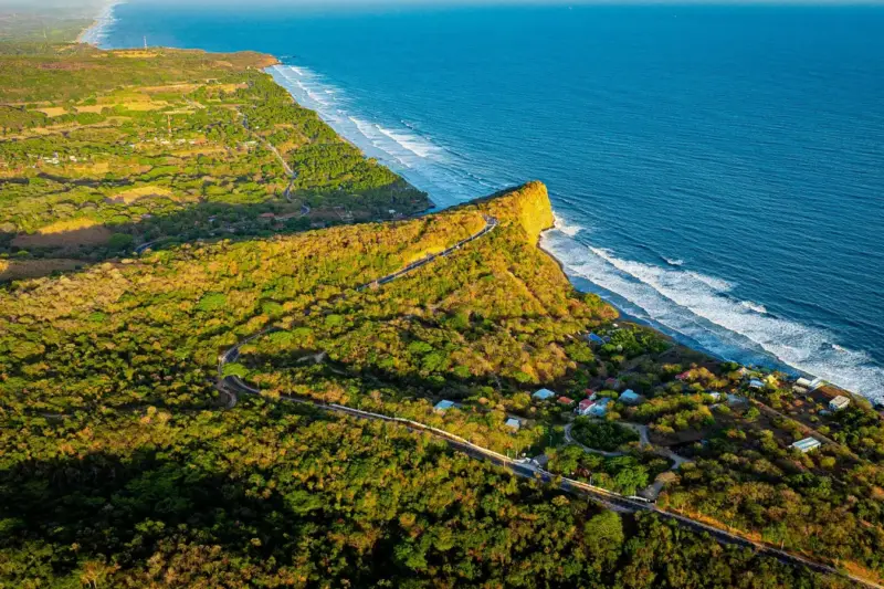 Playa de arena en la costa del Pacífico salvadoreño al atardecer, con surfistas caminando hacia el mar