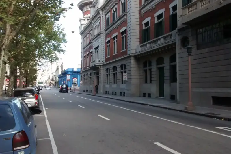 Vendedor ambulante trabajando en una calle de barrio con casas bajas de colores al fondo.
