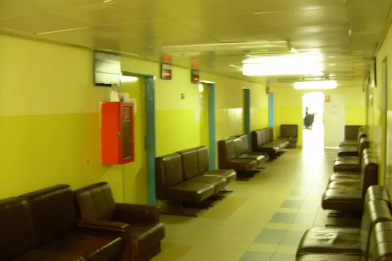 Sala de espera de un centro de salud con luz natural, un papel de cita sobre un banco de madera y una persona mayor al fondo.